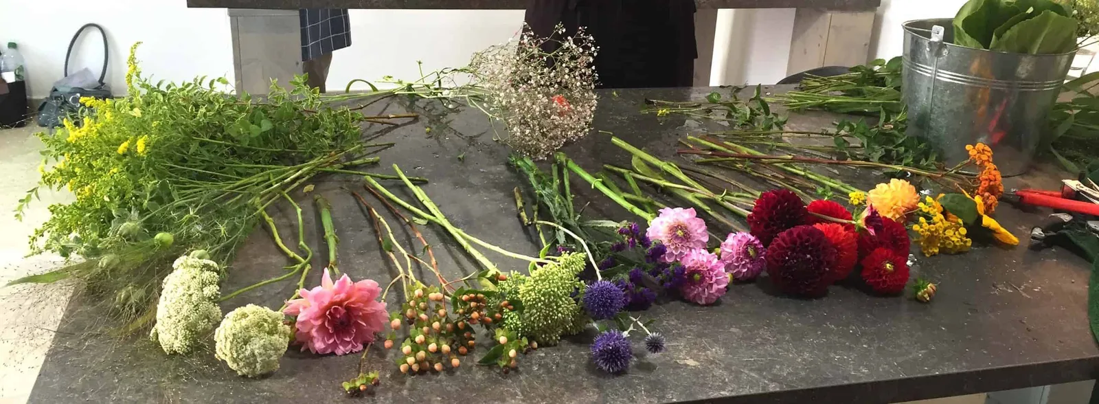 Floristik-Arbeitsplatz mit Schnittblumen und Grünzeug für Gestecke: Dahlien, Nelken, Hypericum, Schleierkraut, Gräser und Bla
