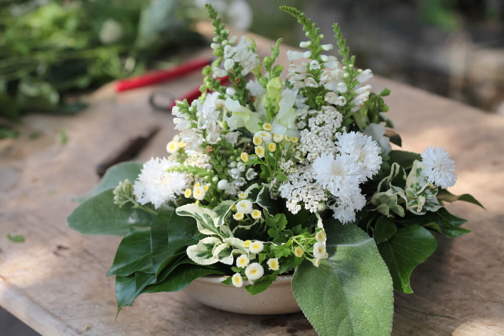 Weißes Blumengesteck mit Gerbera, Kamille und grünen Blättern in Keramikschale