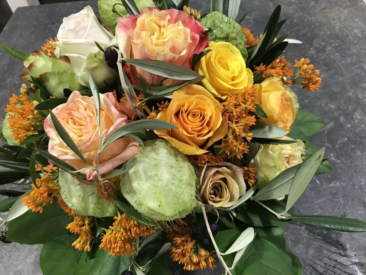Blumenstrauß mit cremefarbenen und gelben Rosen, orangen Akzenten und grünem Laub