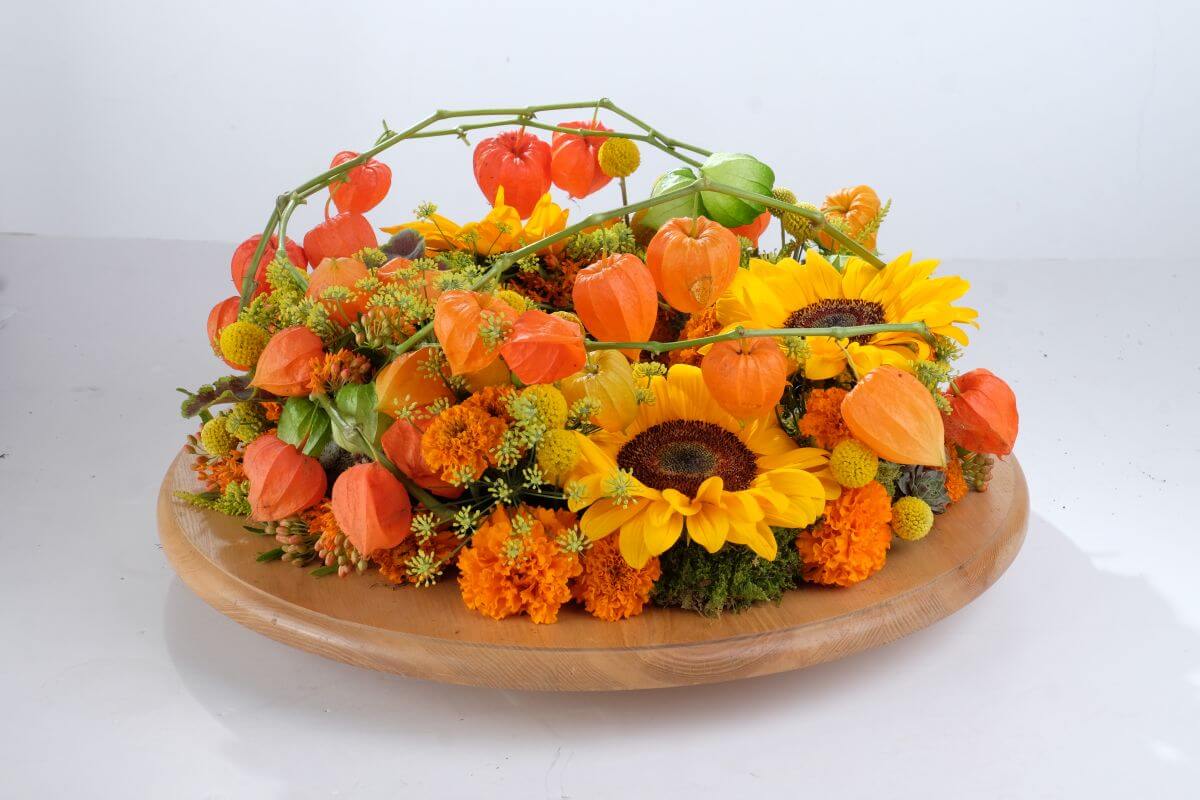 Herbstlicher Kranz auf Holzplatte mit orangefarbenen Lampionblumen, gelben Sonnenblumen und grüner Deko