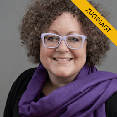 Porträt von Tanja Peters, Frau mit lockigem braunem Haar und Brille in violettem Schal