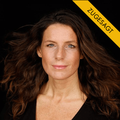 Katharina Pommer, Frau mit braunem lockigem Haar, schwarzem Anzug, vor schwarzem Hintergrund