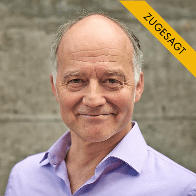 Holger Eckstein, älterer Mann mit grauem Haar, hellviolettem Hemd, vor grauem Hintergrund