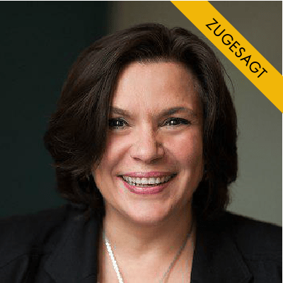 Christine Hofmann, Frau mit dunklem Haar, schwarzem Blazer, hellblauem Oberteil, vor dunklem Hintergrund