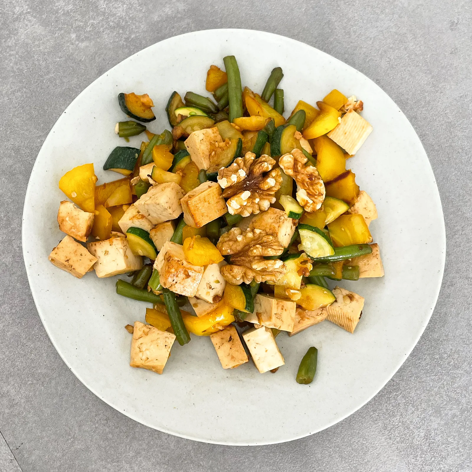Veggie Stir Fry mit Tofu, grünen Bohnen und Walnüssen auf weißem Teller