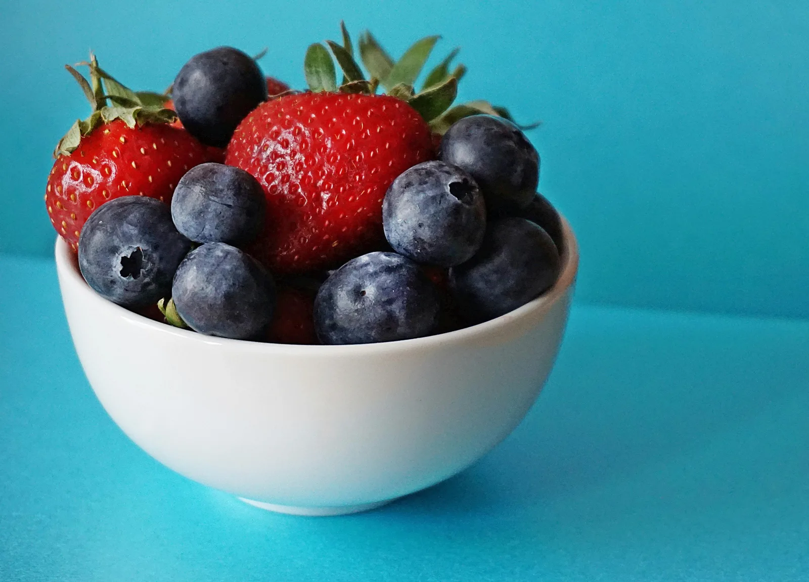 Weiße Schale mit Erdbeeren und Blaubeeren vor hellblauem Hintergrund
