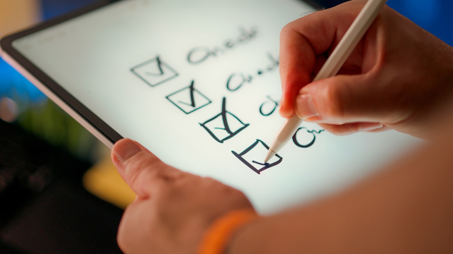 Nahaufnahme Tablet mit Stift beim Abhaken von Kontrollkästchen in Checkliste