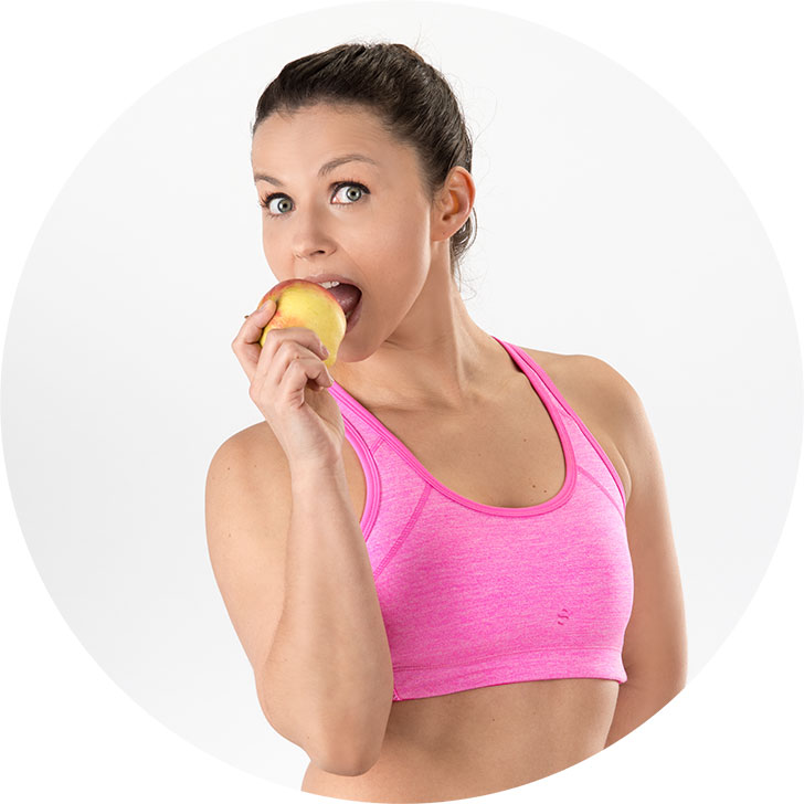 12 Wochen Fatburner Abnehmprogramm – Videokurs zum Abnehmen 3 Frau in pinkem Sport-Top beißt in einen gelben Apfel