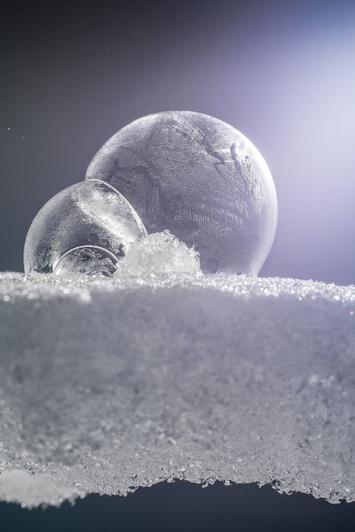 Gefrorene Seifenblasen auf Schnee vor blauviolettem Himmel, Eiskristalle