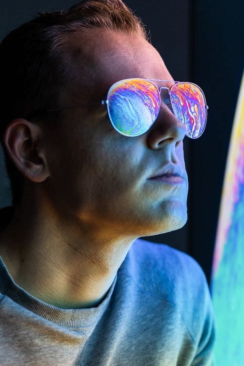 Mann mit bunten Spiegelungen in Sonnenbrillen-Gläsern, farbenfrohe Licht-Effekte