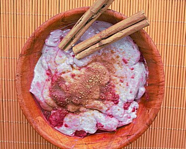 Rosa Açai Bowl mit roten Beeren und Zimtstangen in Holzschale