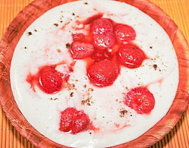 Weiße Schale mit roten Himbeeren und Kakao-Pulver auf orangefarbener Matte