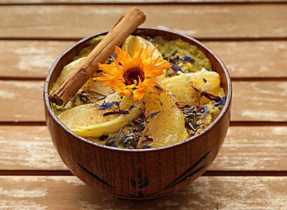Holzschale mit Müsli, Apfelscheiben, Blüte und Zimtstangen