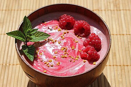 Rosa Pudding mit Himbeeren und Sprösslingen in brauner Schale auf Bambusmatte
