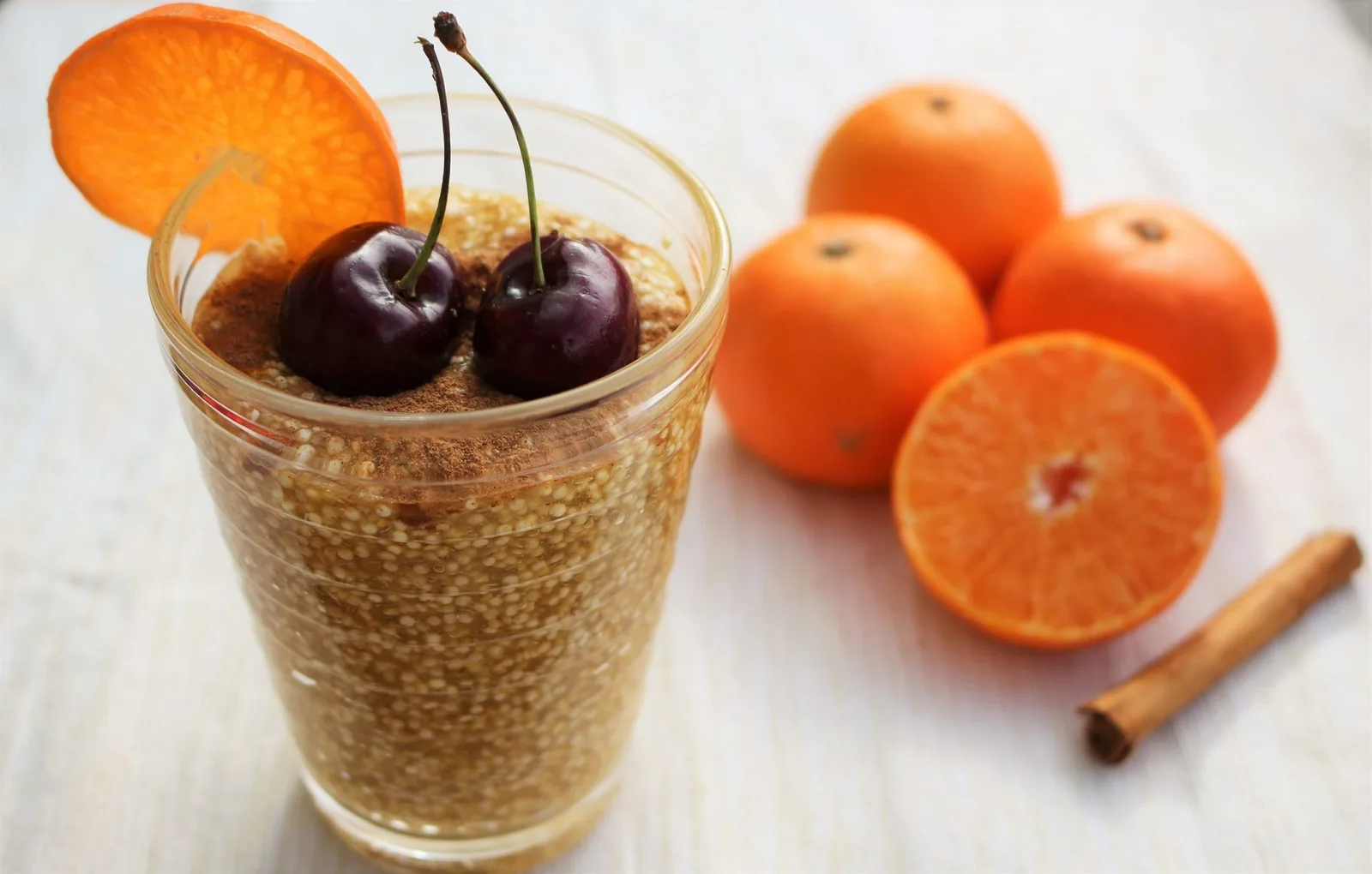 Chia-Pudding mit Kirschen, Orangenscheiben und Zimtstangen im Glas