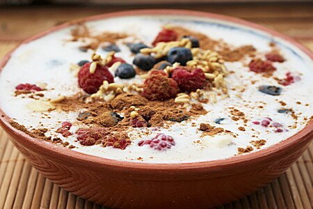 Haferbrei mit Beeren und Müsli in heller Schale auf Bambusunterlage