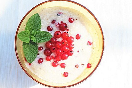 Creme-farbenes Dessert mit roten Johannisbeeren und Minzblatt in Schale