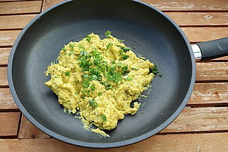Rührei mit Kräutern in schwarzer Pfanne auf Holztisch