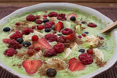 Grüner Smoothie Bowl mit Beeren und Trockenobst garniert