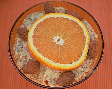Müslischale mit Orangenscheibe und Mandeln auf oranger Bambusmatte