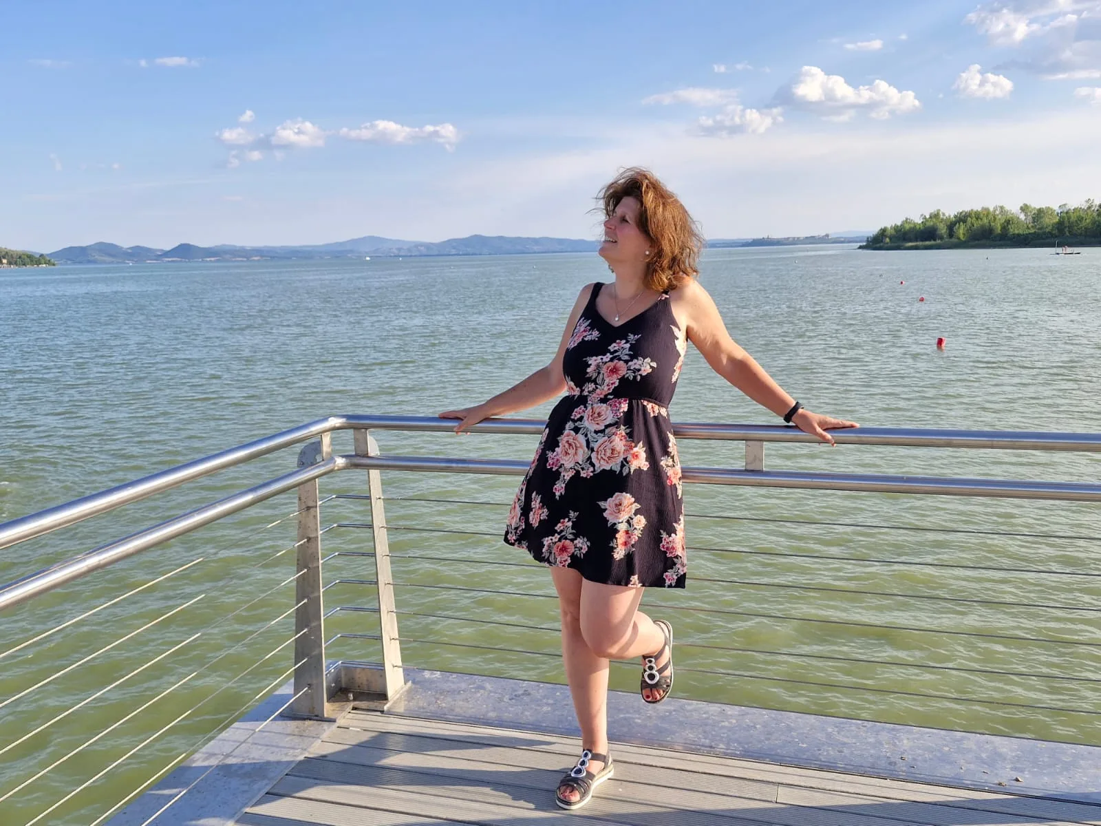 Frau in Blummenkleid am See mit Bergen und Himmel