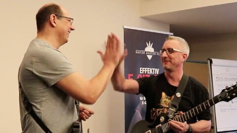 Zwei Männer, einer mit Gitarre, einer klatscht, lächelnde Atmosphäre beim Jammen