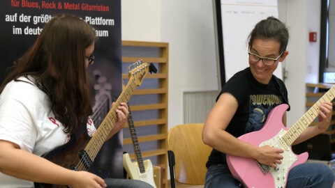 Zwei junge Frauen spielen rosa und schwarze Gitarren zusammen, Spaß beim Jammen