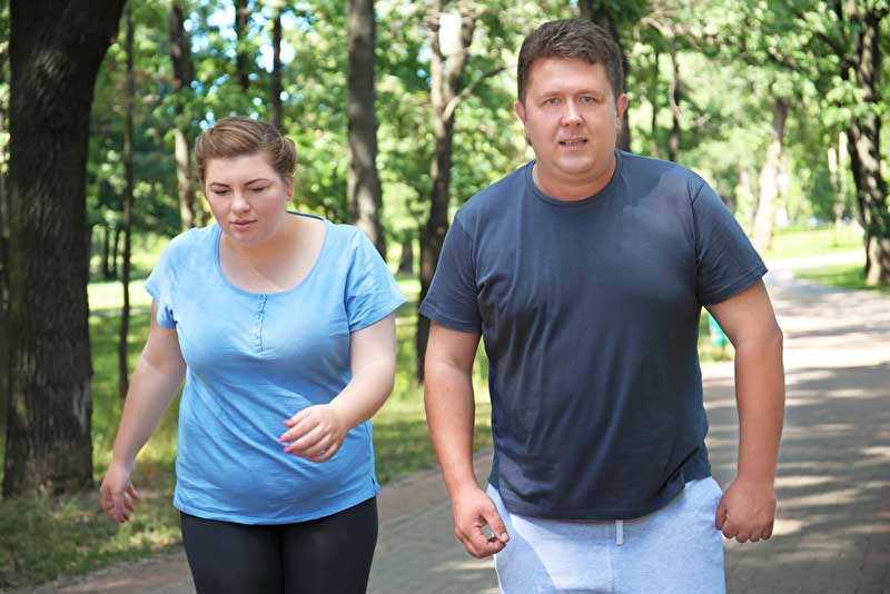 Frau und Mann joggen zusammen auf Weg durch grüne Allee
