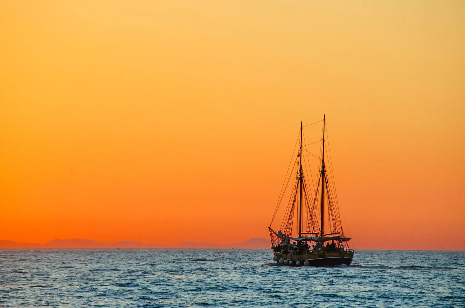 Zweimastige Segelyacht auf dem Meer bei Sonnenuntergang mit orangegoldenem Himmel