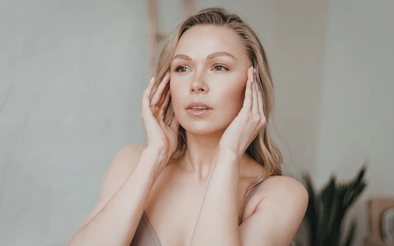 Frau mit heller Haut berührt ihr Gesicht, minimalistischer grauer Hintergrund