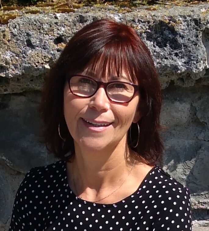Katharina, Frau mit Brille und dunklen Haaren vor Steinwand