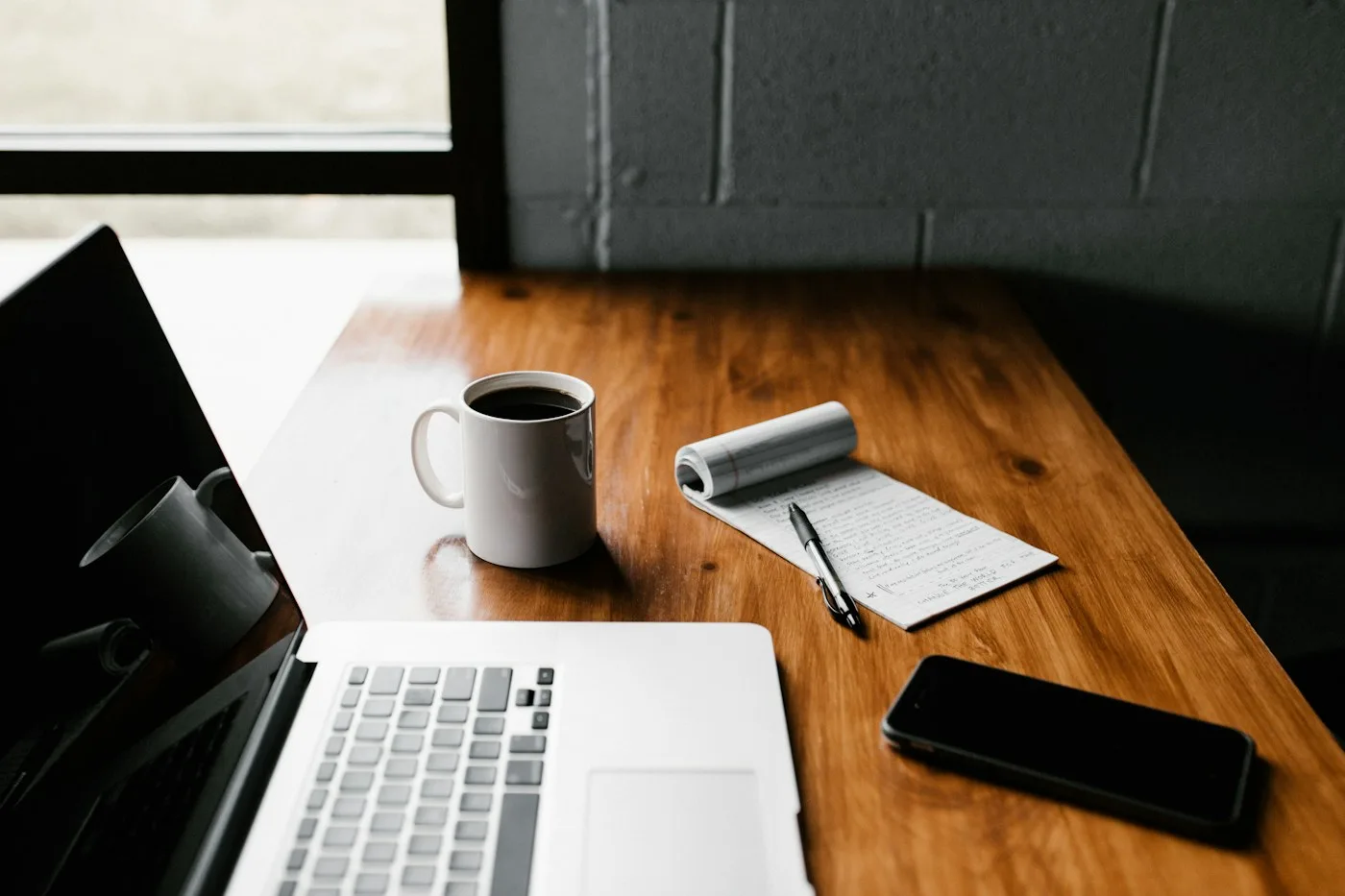 Schreibtisch mit Laptop, Notizbuch, Kaffeetasse und Smartphone in Holzoptik