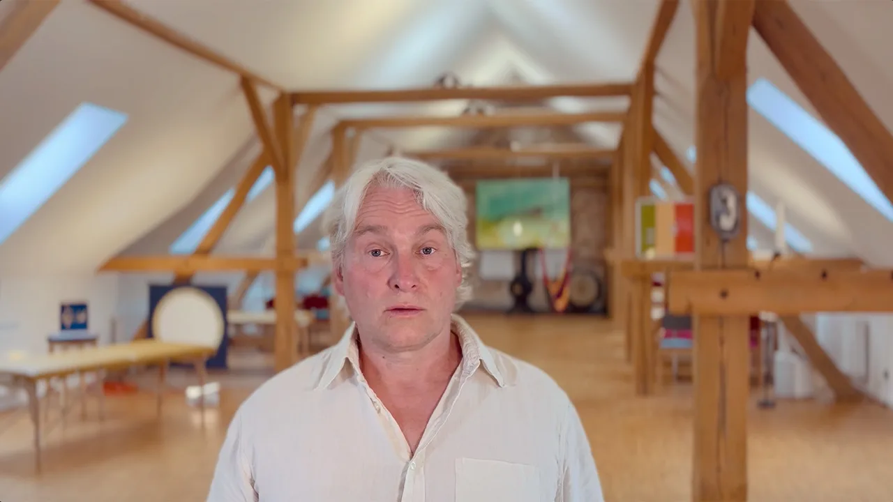 Uwe Albrecht spricht in hellem Dachraum mit Holzbalken und Fenster – Videostandbild