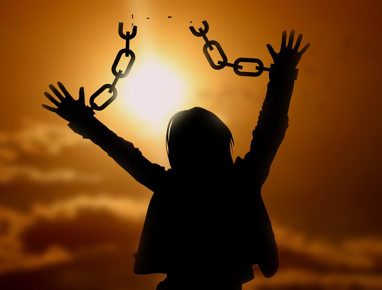 Silhouette einer Person mit erhobenen Armen befreit sich von Ketten vor goldenem Himmel, Freiheit und Befreiung