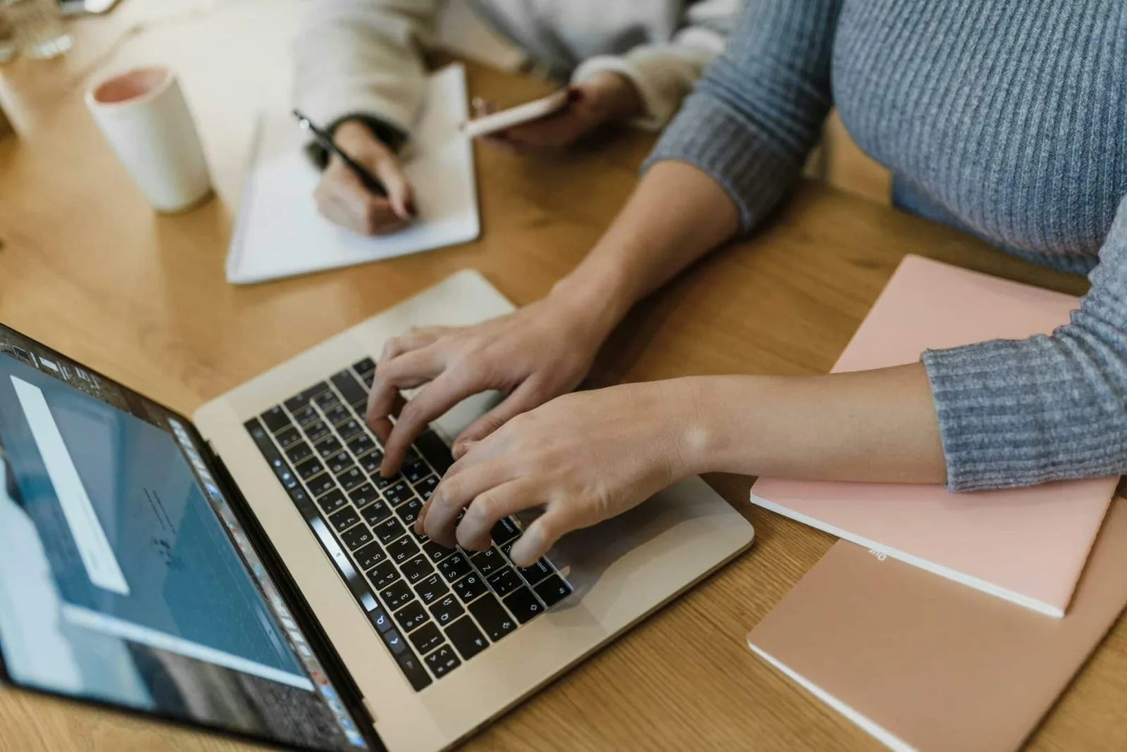 Hände einer Person am Laptop-Trackpad, Arbeitsumgebung mit Notizpapieren und Kaffee sichtbar