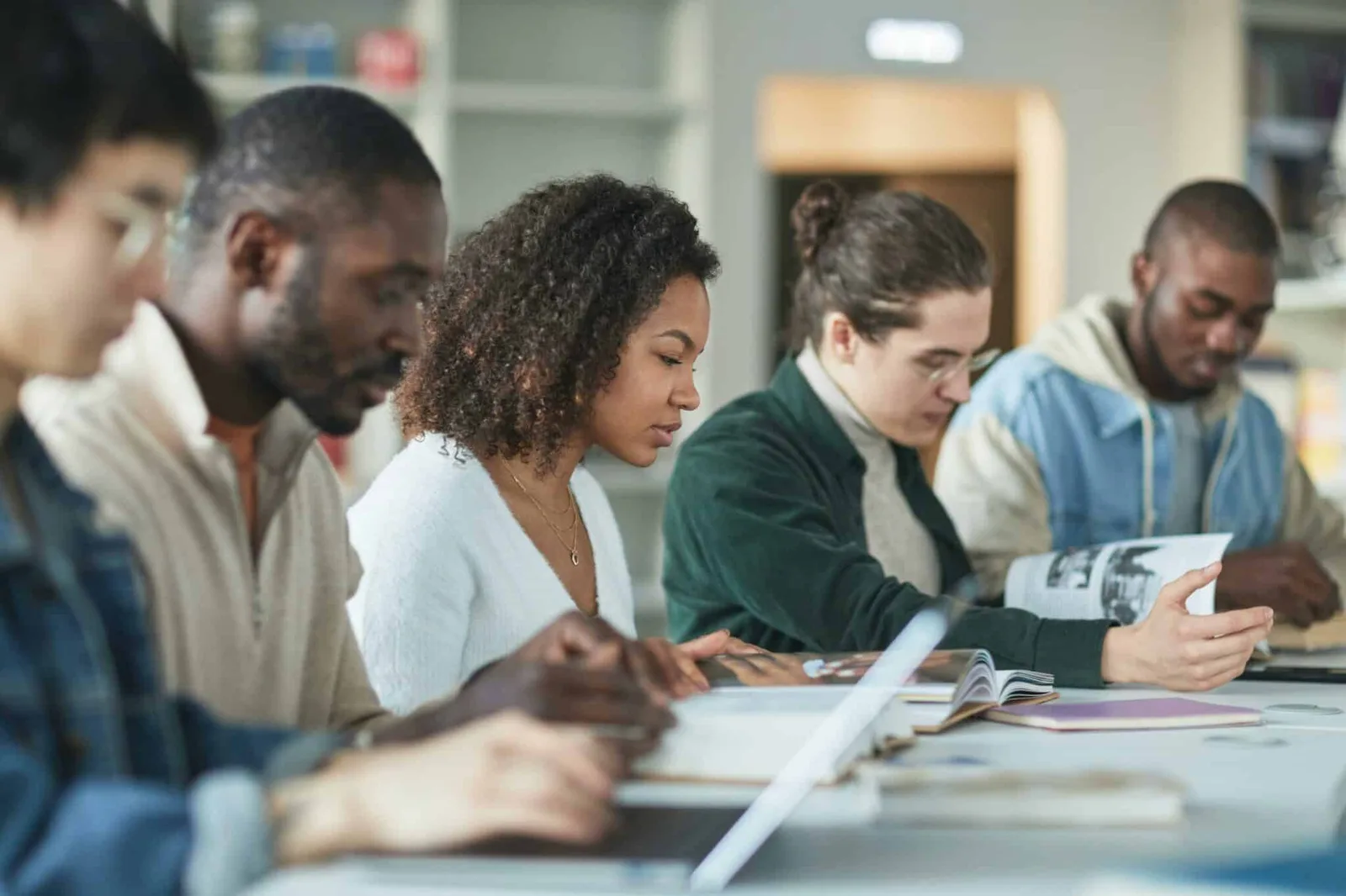 Diverse Gruppe von fünf Personen sitzt zusammen an einem Tisch und studiert gemeinsam Materialien