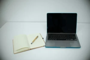 Laptop und leeres Notizbuch mit Stift auf weißem Tisch, Planung und Strategie