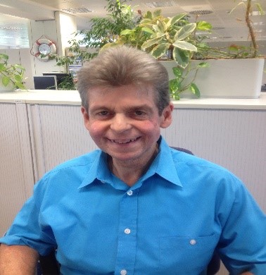 Porträtfoto von Jürgen Luber in blauem Hemd im Büro lächelnd
