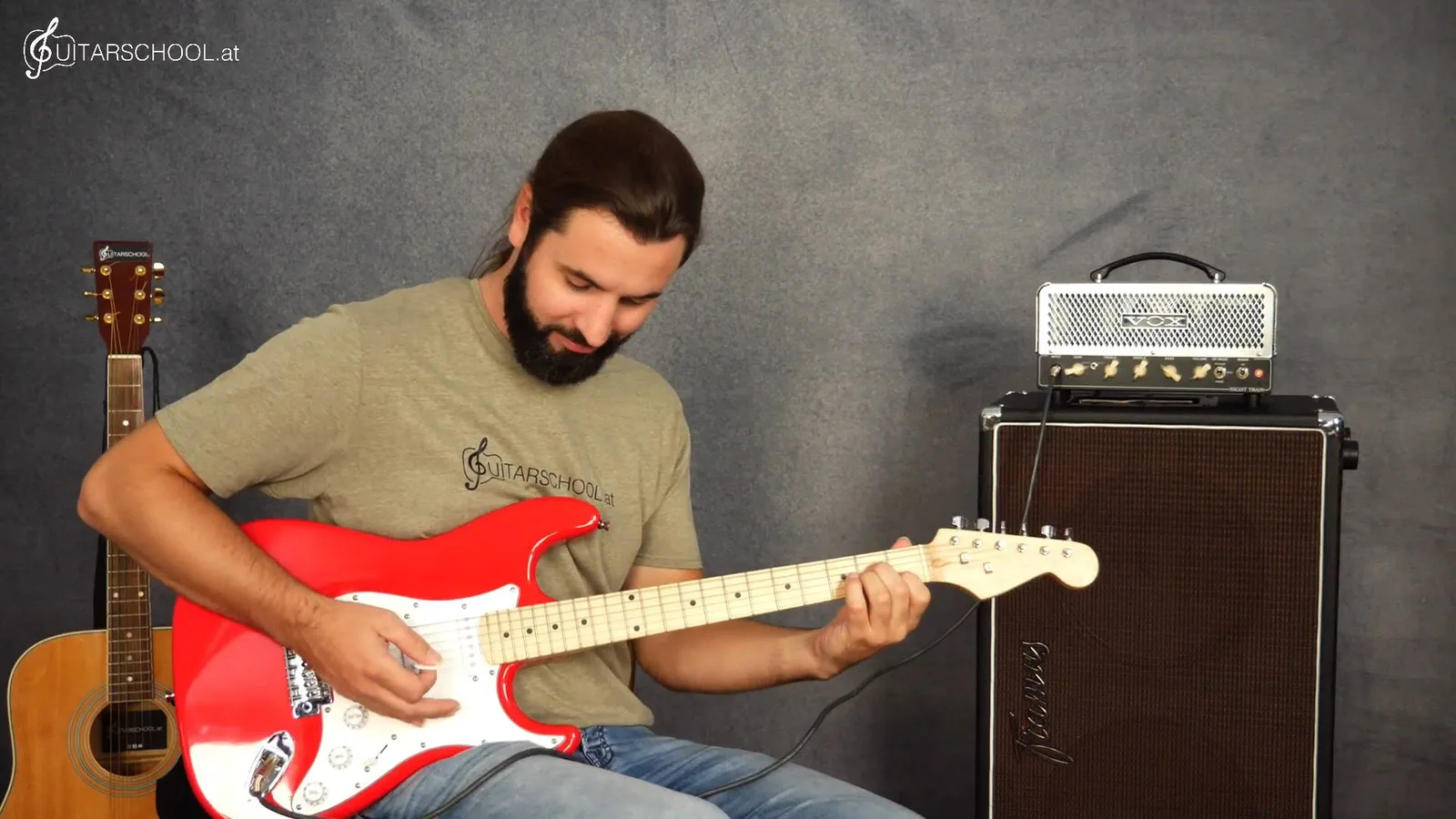 Gitarrenlehrer spielt rote E-Gitarre mit Verstärker im Hintergrund – E-Gitarren-Unterricht