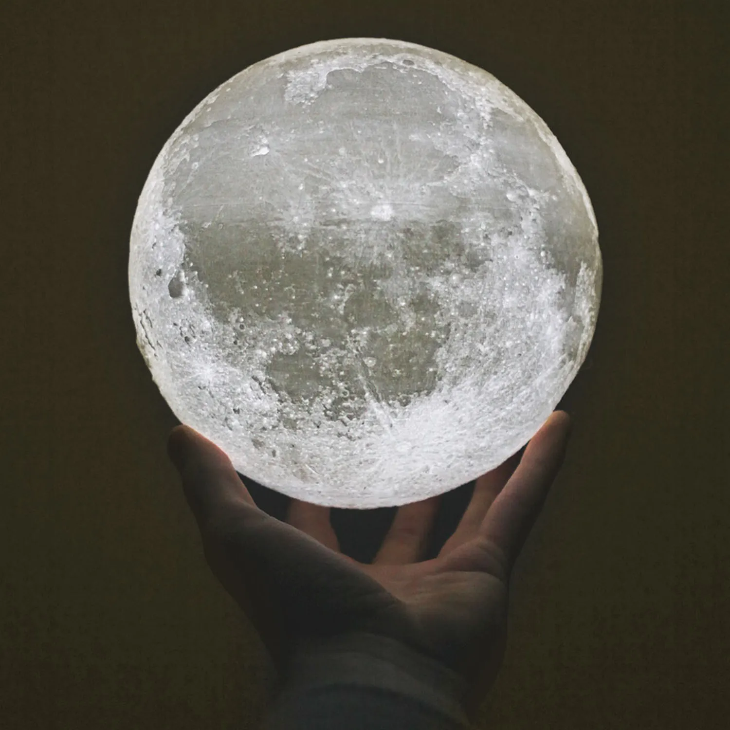 Hand hält leuchtenden Vollmond vor dunklem Hintergrund