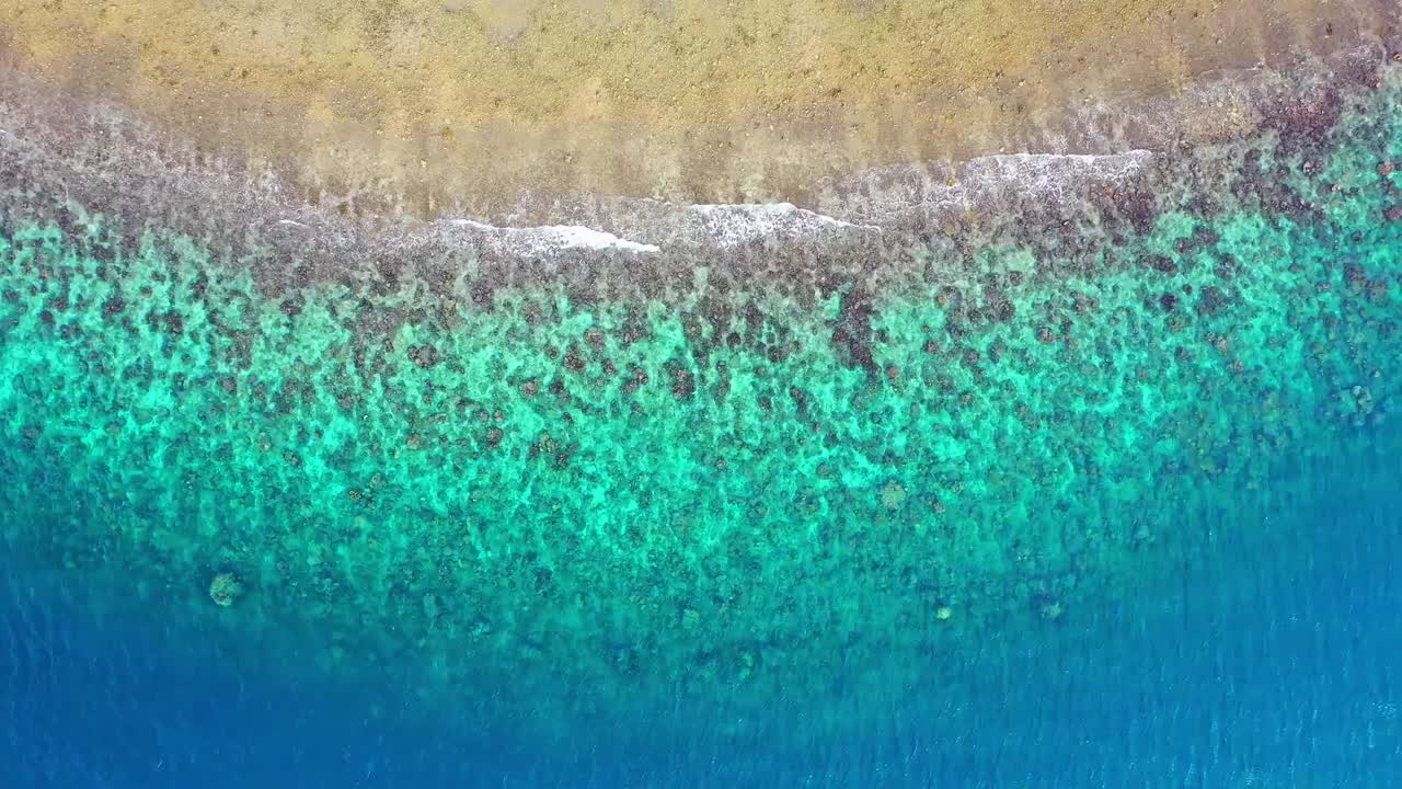 Luftaufnahme eines sandigen Strandes mit türkisblauem Wasser und Riffen
