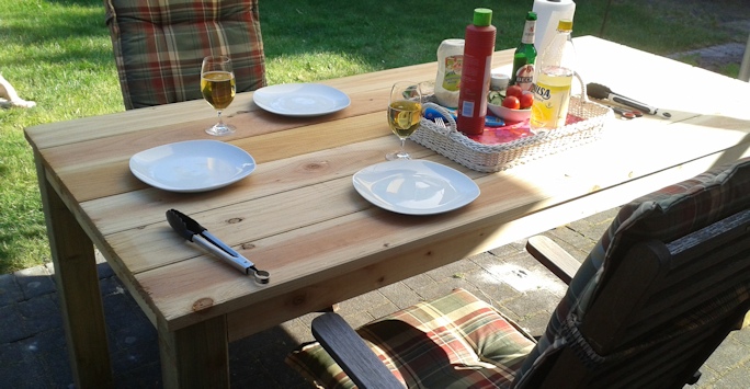 Anleitung Gartentisch bauen – PDF-Ratgeber zum Möbelbau aus Holz 7 Selbstgebauter Gartentisch mit Essen: Teller, Glas und Besteck auf Holztisch