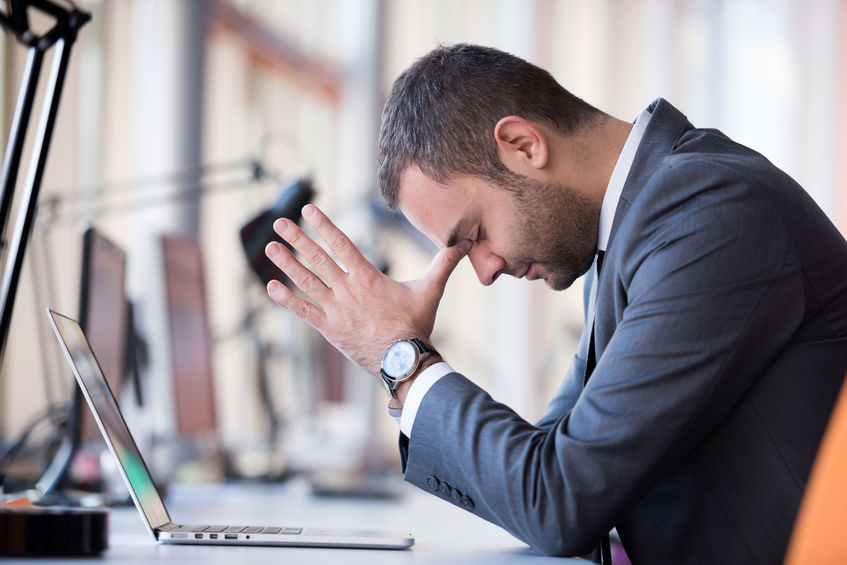 Mann im Anzug sitzt am Laptop, Hand am Gesicht, Frustration oder Konzentration