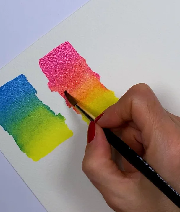 Hand mit Pinsel malt bunte Aquarell-Farbverläufe in Blau, Pink, Orange und Gelb