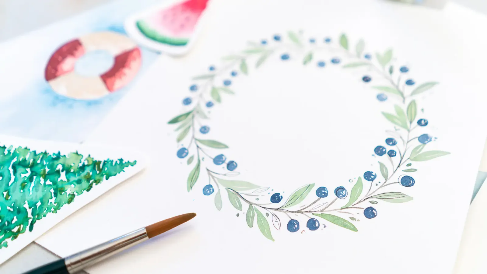 Aquarell-Zeichnungen mit Früchten und blauem Beerenblätterkranz mit Pinsel und Aquarellpalette