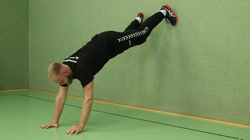 Trainerin führt Handstand-Push-up-Übung auf grünem Volleyballfeld durch