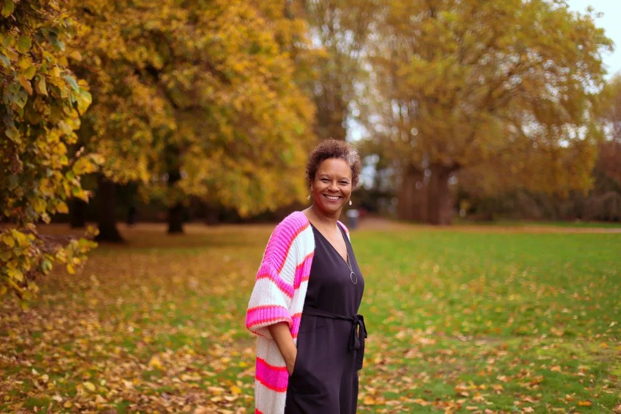 Frau in rosa-weiß gestreifter Strickjacke und schwarzem Kleid in Herbstpark mit gelben Blättern