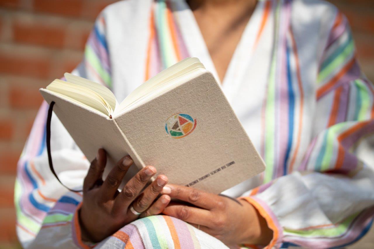 Hände halten offenes Buch mit geometrischem Symbol, bunte Streifenjacke