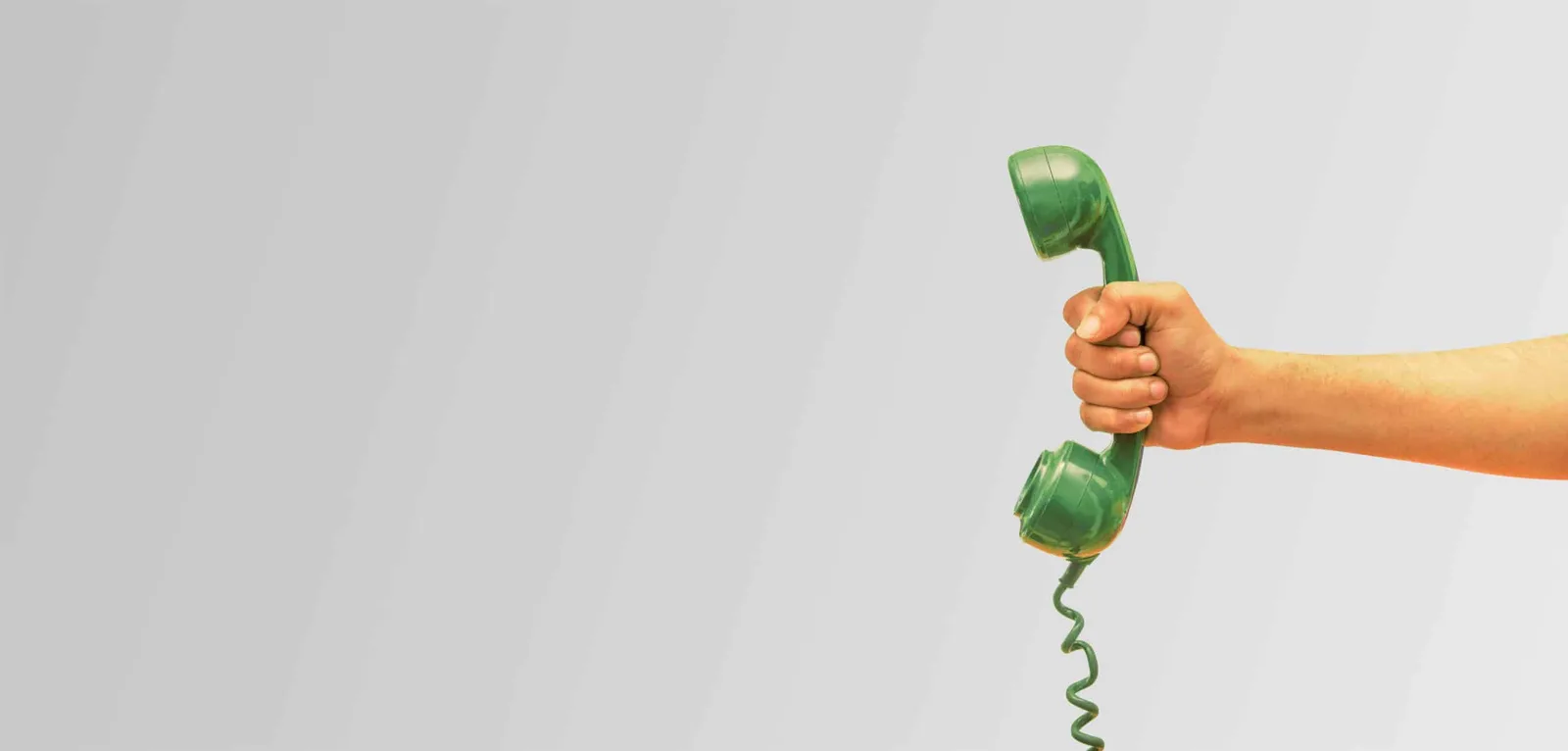 Hand hält grünen Telefonhörer auf hellgrauem Hintergrund