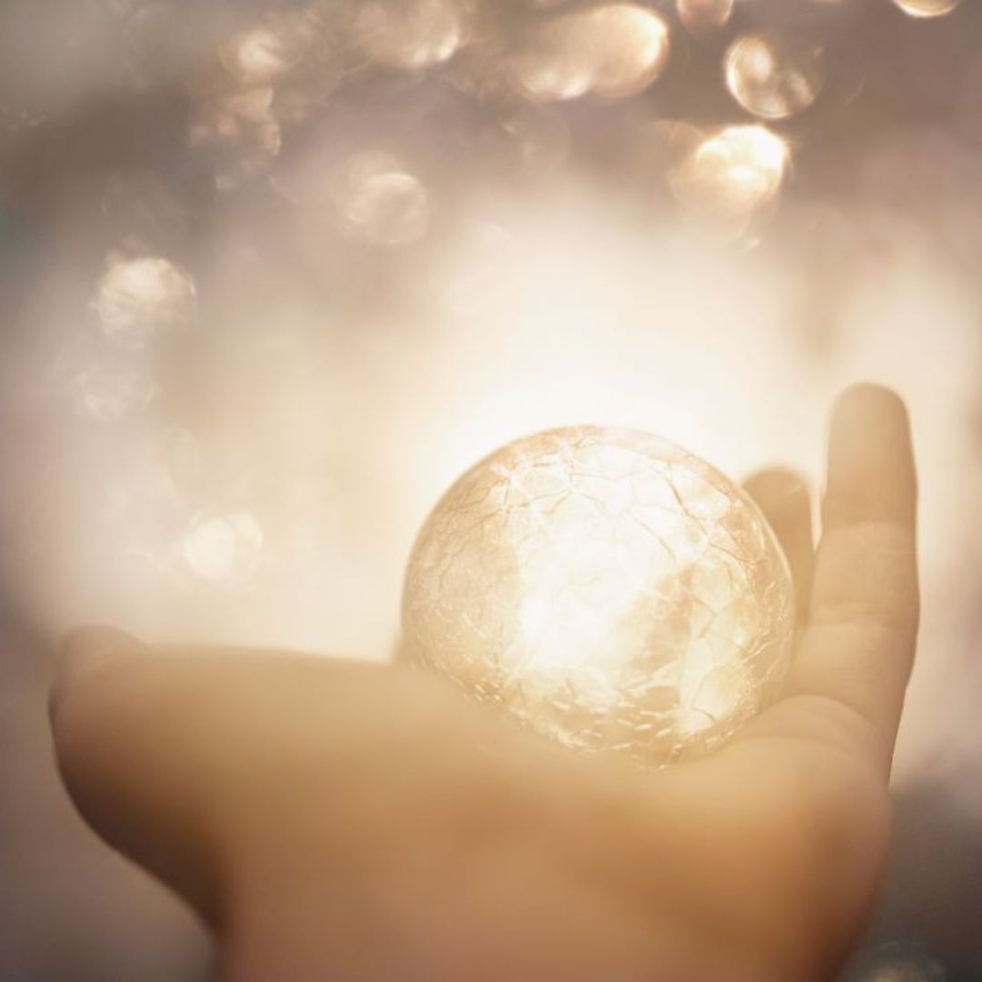 Hand mit leuchtender Kugel, Bokeh-Lichter im Hintergrund, symbolisiert innere Kraft und Licht